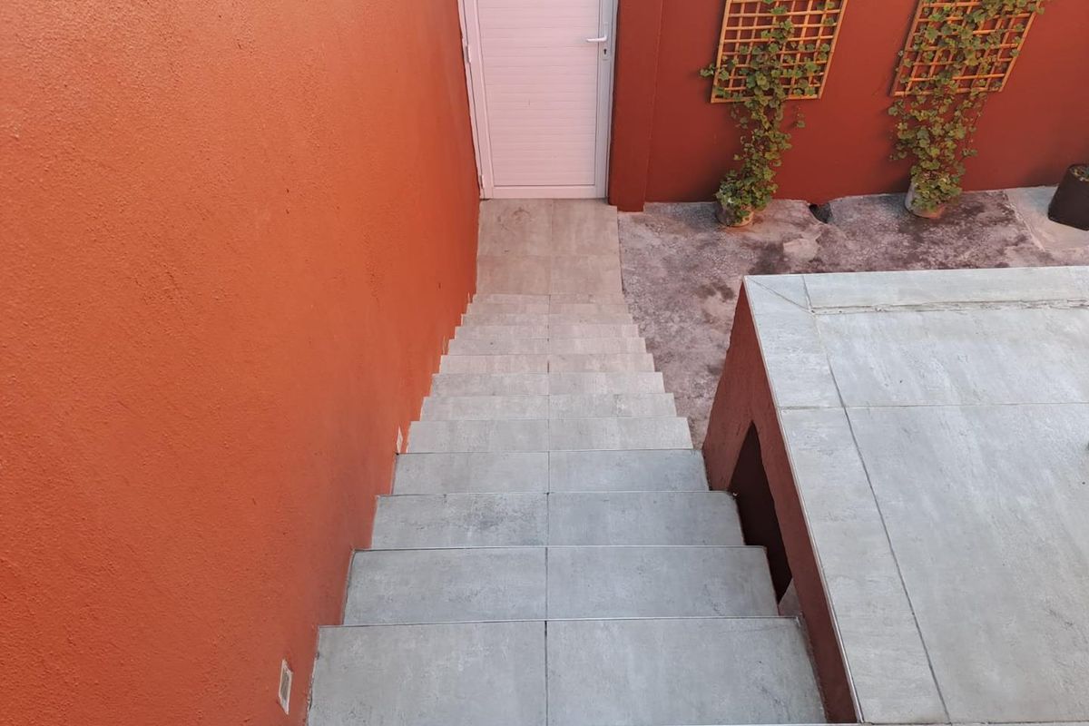 An outdoor staircase with tiled steps leading down to a small courtyard area with terracotta-colored walls and decorative wooden trellises.