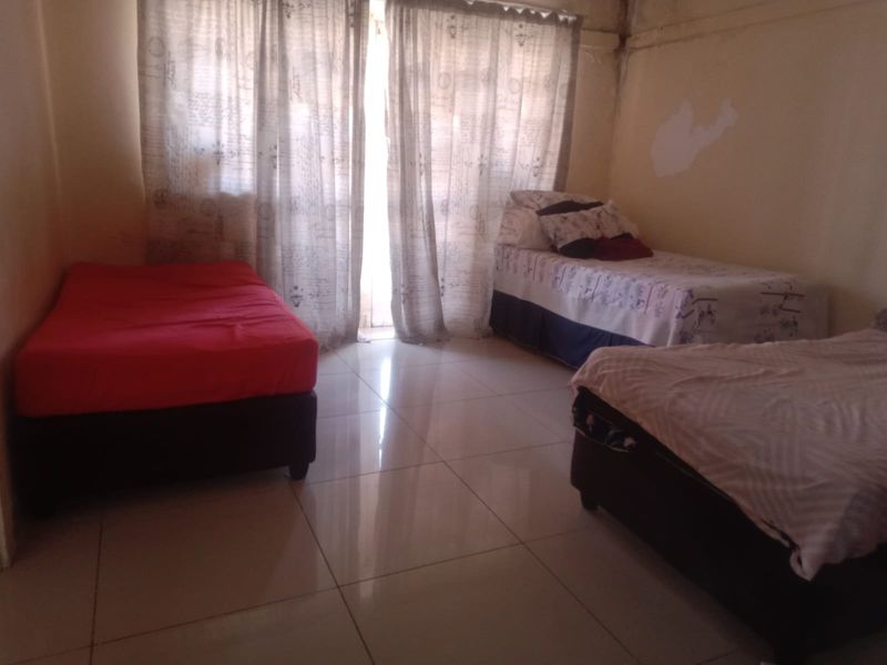A bedroom featuring tiled flooring and large windows with curtain rails, currently showing signs of wall surface wear and paint deterioration.