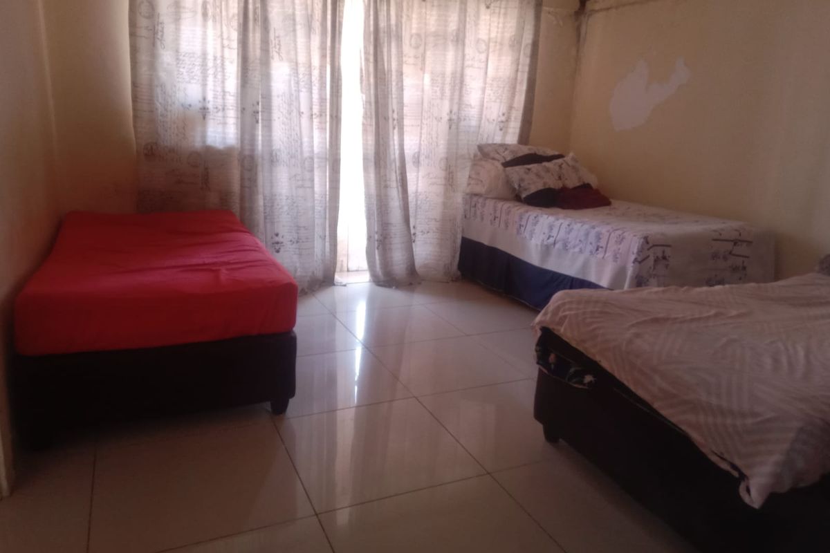 A bedroom featuring tiled flooring and large windows with curtain rails, currently showing signs of wall surface wear and paint deterioration.