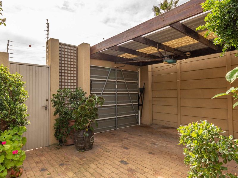 A paved outdoor parking area featuring a timber pergola, secure garage door, and perimeter wall with electric fencing.