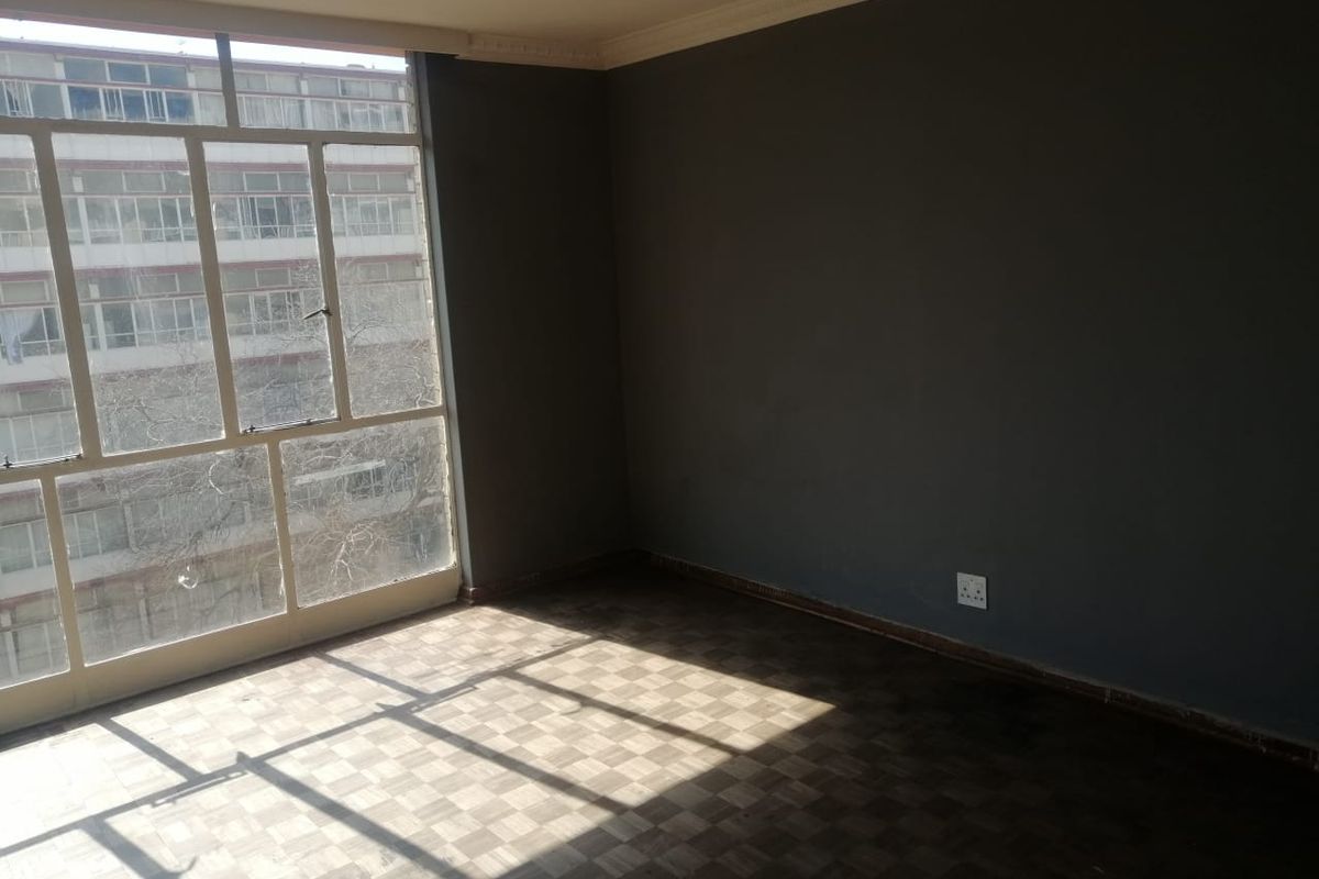 An empty bedroom featuring large metal-framed windows, parquet flooring, and decorative ceiling cornices, offering a blank canvas for personalization.