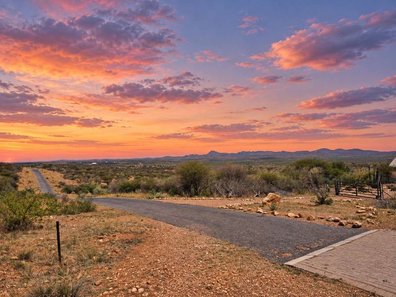 A scenic view of the surrounding landscape and horizon at sunset, featuring a paved driveway leading into the property.
