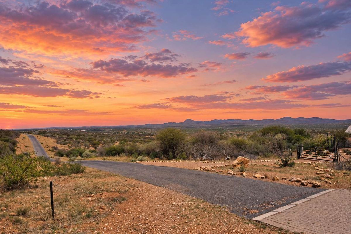 A scenic view of the surrounding landscape and horizon at sunset, featuring a paved driveway leading into the property.