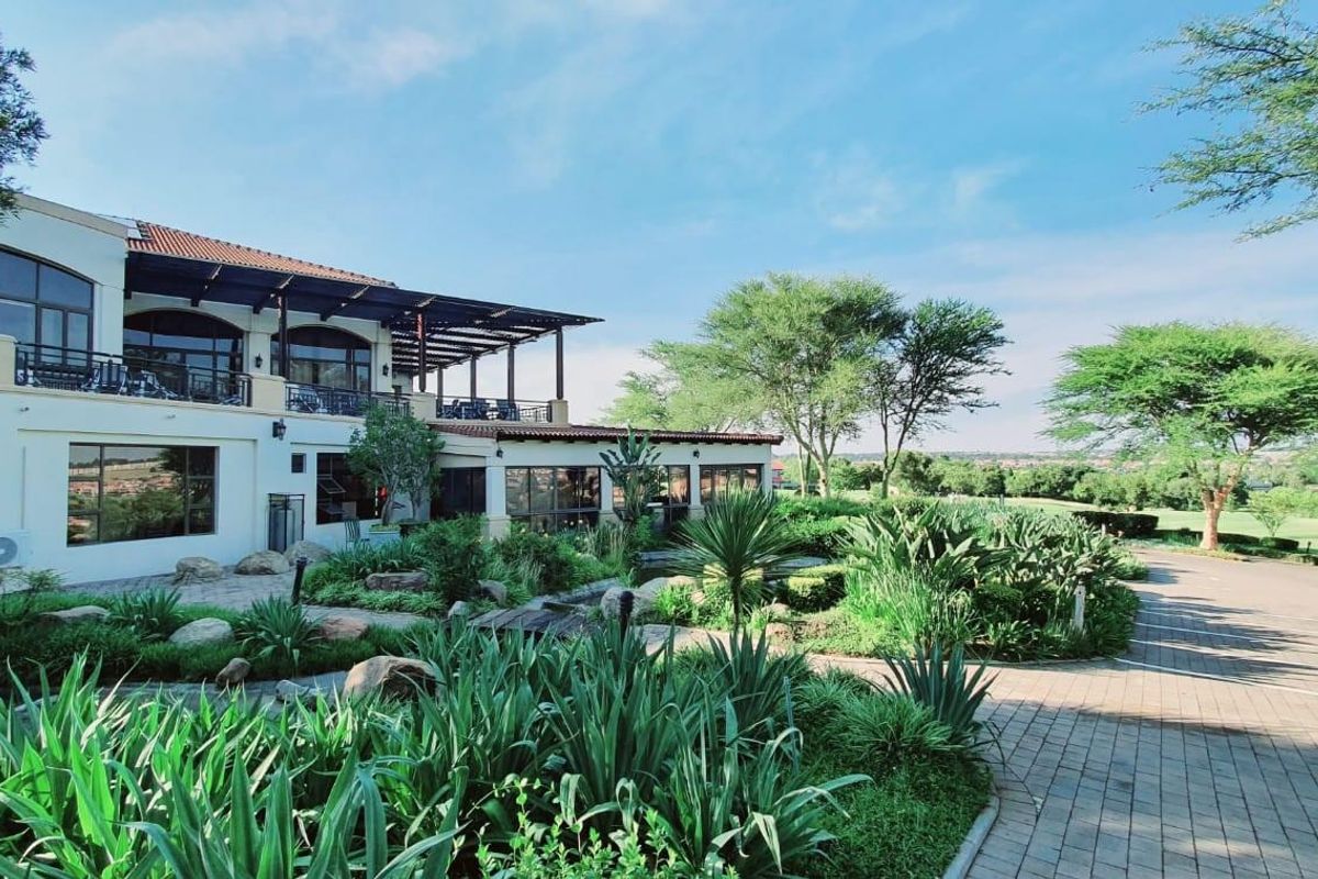 A view of the rear exterior of a large residential property featuring a covered patio, landscaped garden, and paved driveway area.