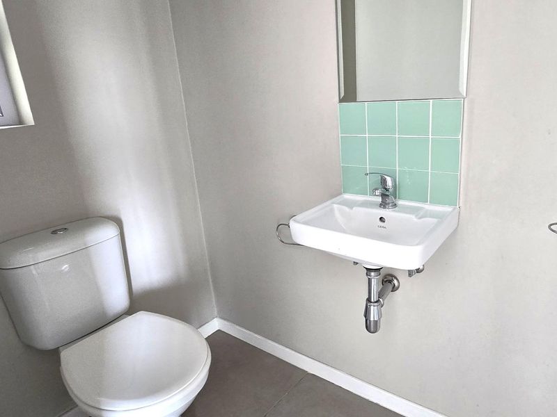 A clean and functional guest bathroom featuring a wall-mounted basin with a tiled splashback, a standard toilet, and neutral wall finishes.
