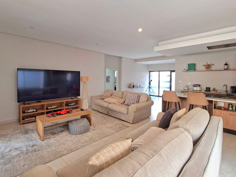 Spacious open-plan living area featuring a modern kitchen with island, recessed lighting, and seamless flow to the outdoor patio through sliding glass doors.