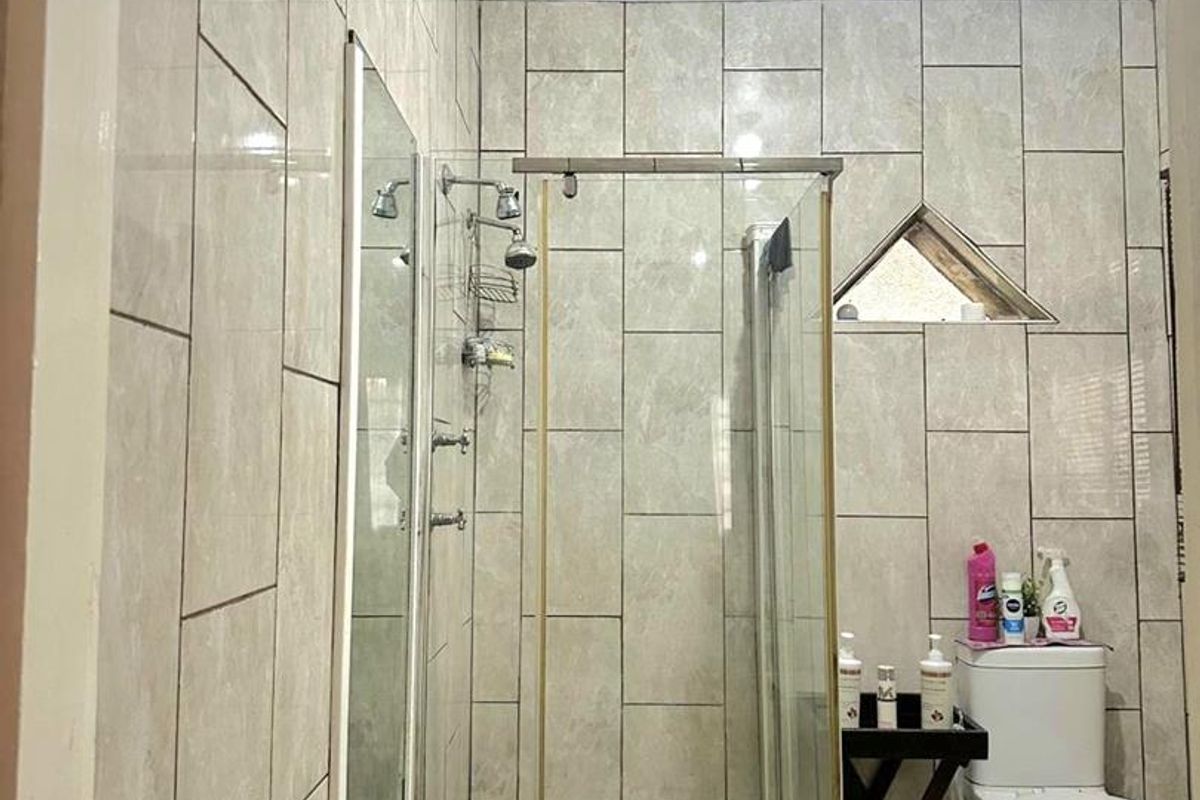 A functional bathroom featuring a glass-enclosed shower, tiled walls, and a standard toilet with a unique triangular window.