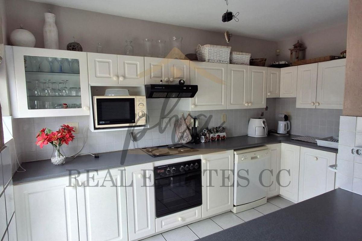 A functional kitchen featuring white cabinetry, a built-in oven, extractor fan, and tiled flooring, offering a practical layout for daily meal preparation.
