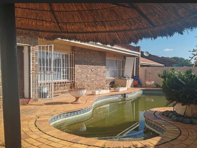 Outdoor pool area featuring a thatch lapa, brick paving, and a swimming pool requiring maintenance.