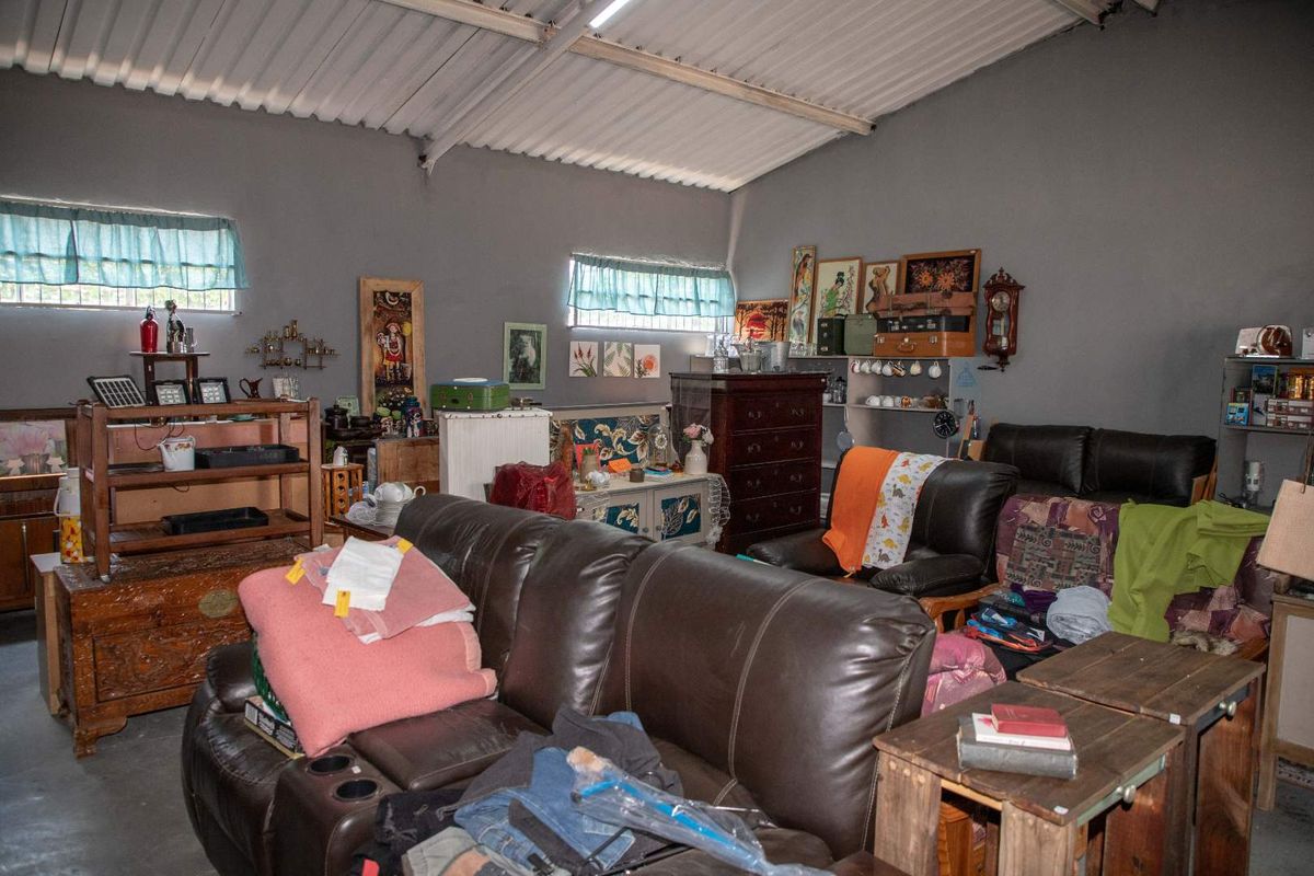 A spacious interior area featuring high exposed ceilings, grey painted walls, and multiple windows, currently utilized as a multi-purpose living or storage space.