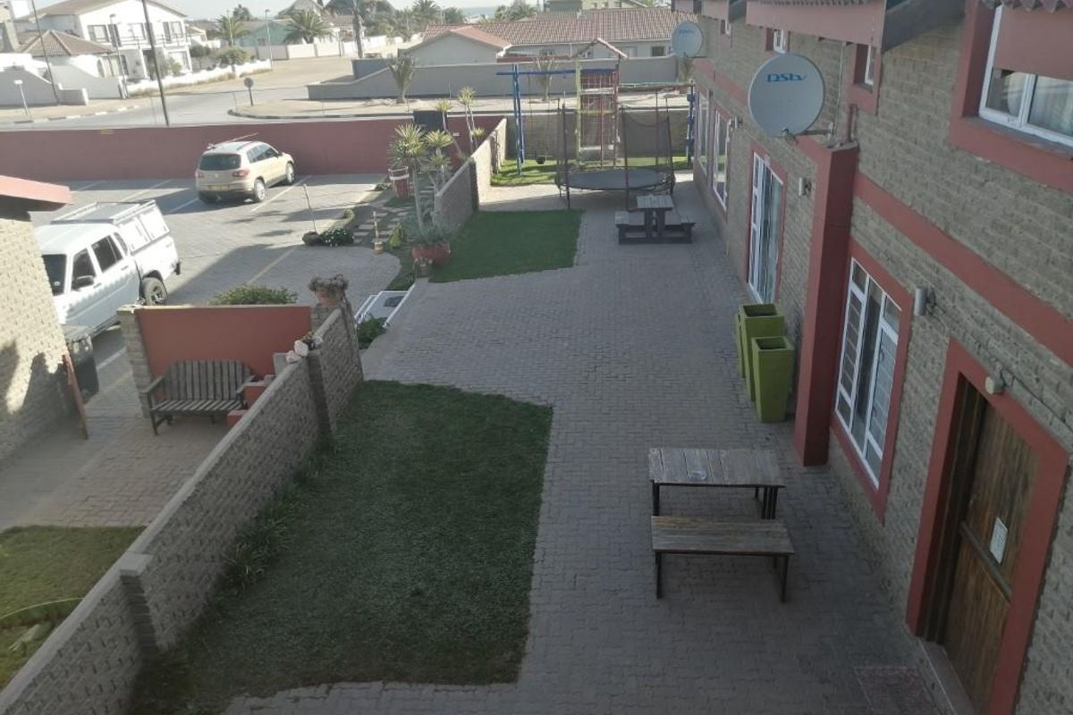 Elevated view of the guest house exterior, featuring a paved courtyard, landscaped lawn patches, and direct access to the parking area.