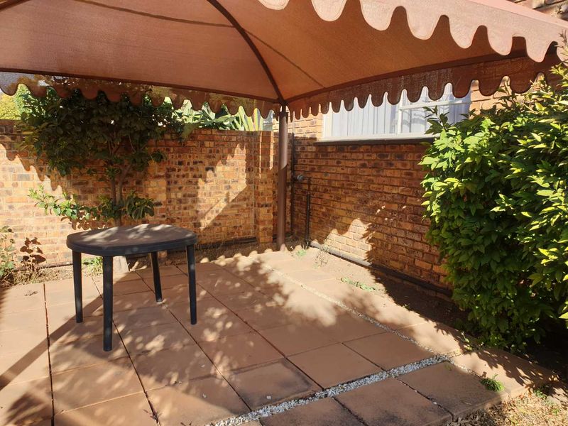 A private outdoor patio area featuring paved flooring, a brick boundary wall, and a fixed metal gazebo structure for shaded outdoor living.