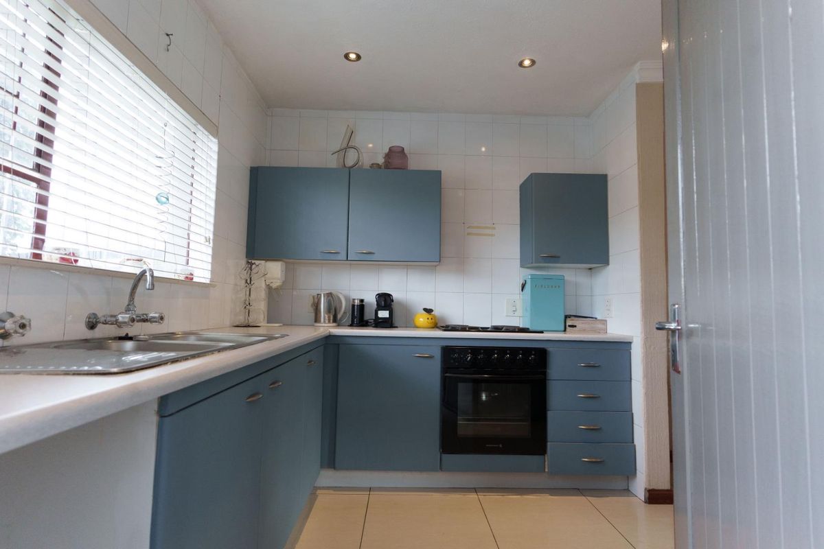 A functional kitchen featuring blue cabinetry, a built-in oven, hob, and a stainless steel sink with tiled splashbacks.