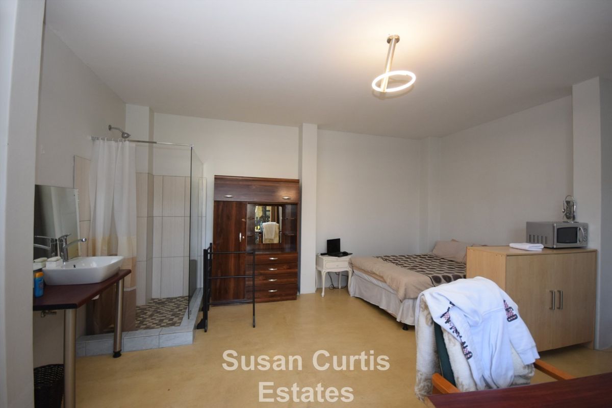 Open-plan bedroom featuring an integrated shower cubicle and vanity basin, providing a functional living space with neutral finishes.