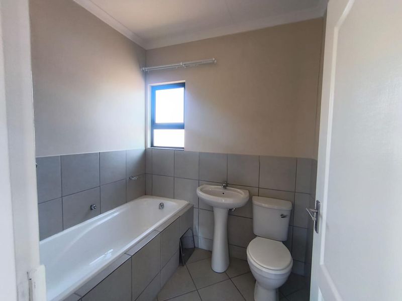 A clean, functional bathroom featuring a bathtub, pedestal sink, and toilet with neutral grey wall and floor tiling.