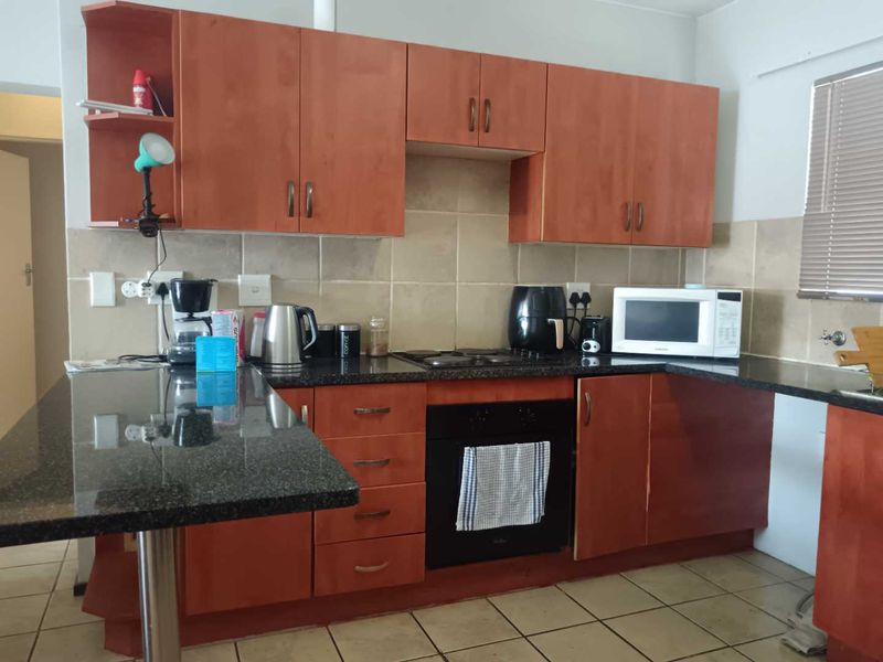 A functional kitchen featuring granite countertops, laminate cabinetry, a built-in oven, electric hob, and a convenient breakfast bar area.