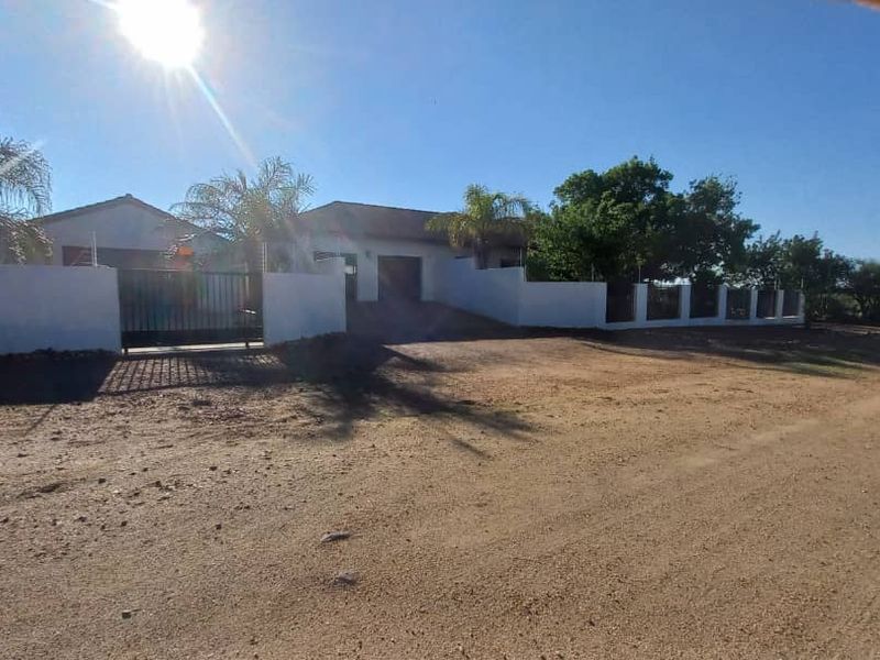 Front exterior view of a residential property featuring a perimeter wall, security gate, electric fencing, and a tiled roof structure.
