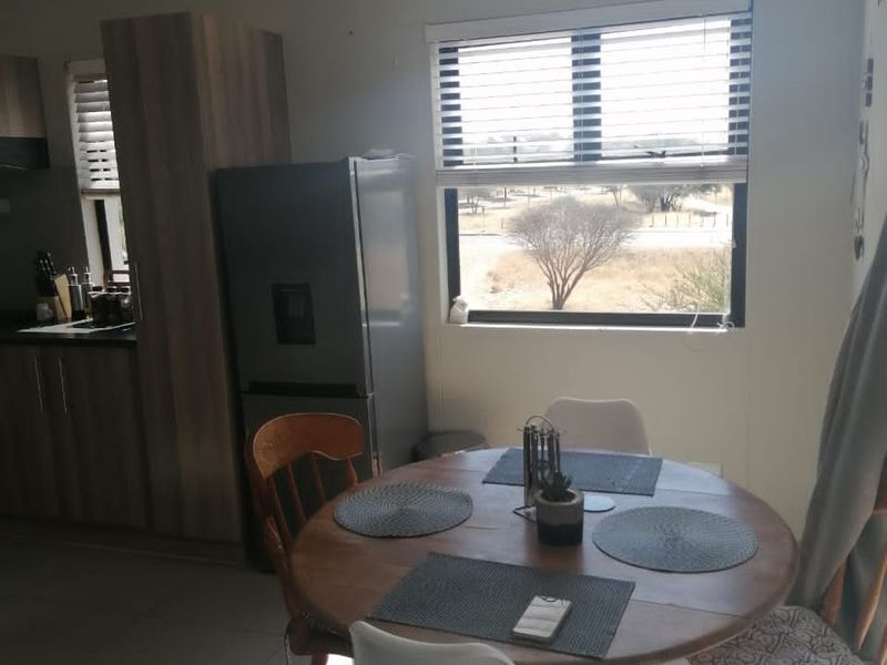 Open-plan living and dining area featuring tiled flooring, modern cabinetry, and large windows with venetian blinds, offering a bright and functional space.