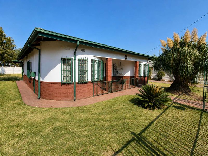 A single-story house featuring a brick facade, covered patio area, and secure metal window bars, set within a well-maintained garden.