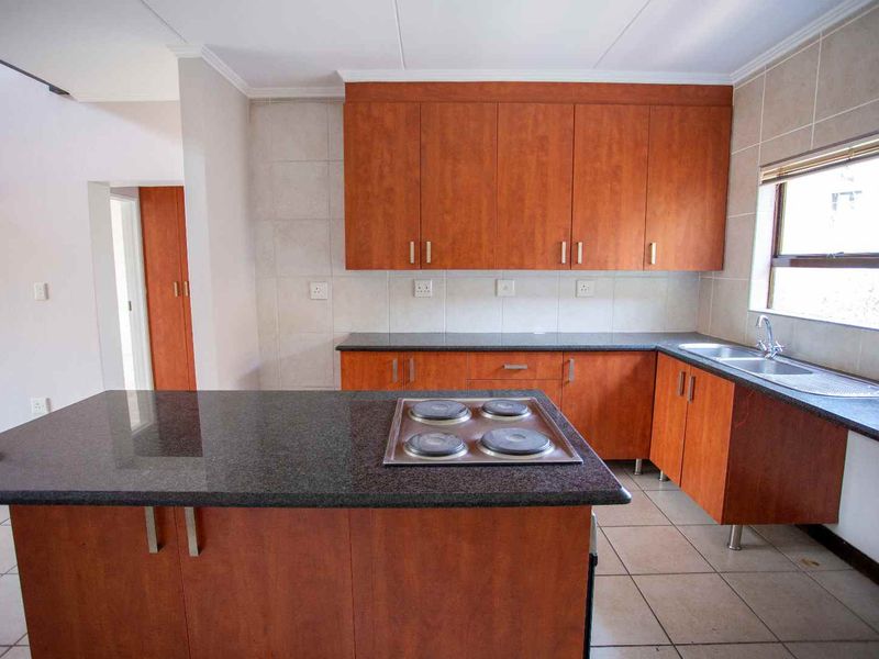 A functional kitchen featuring wood-finish cabinetry, granite countertops, a central island with an integrated electric hob, and tiled flooring.