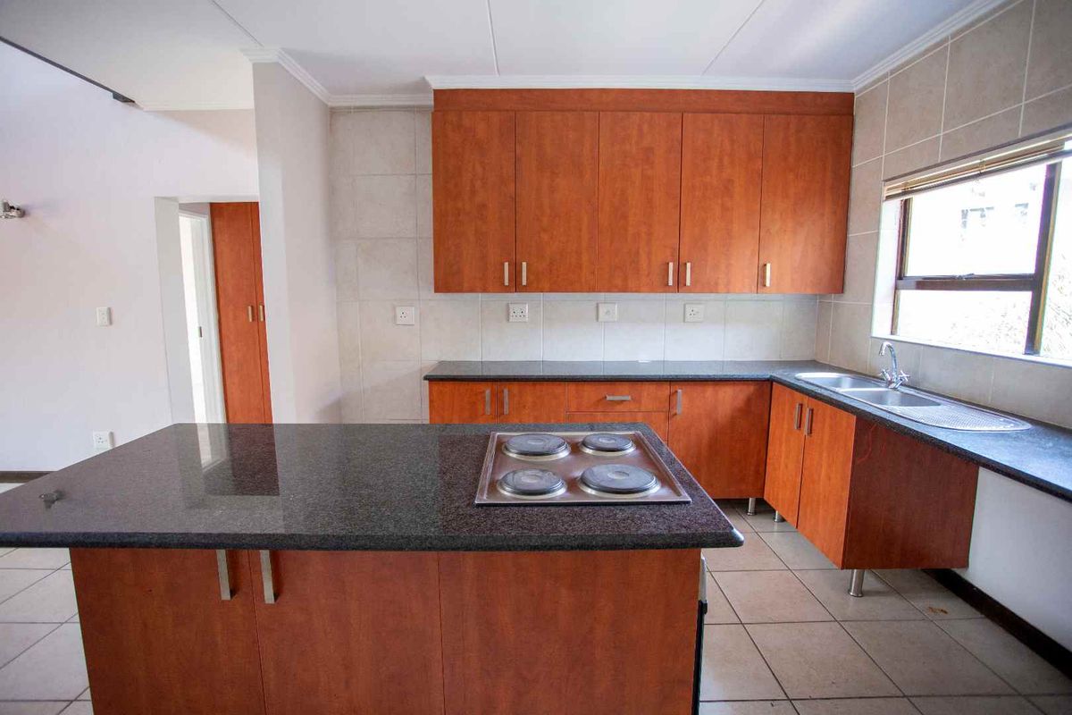 A functional kitchen featuring wood-finish cabinetry, granite countertops, a central island with an integrated electric hob, and tiled flooring.