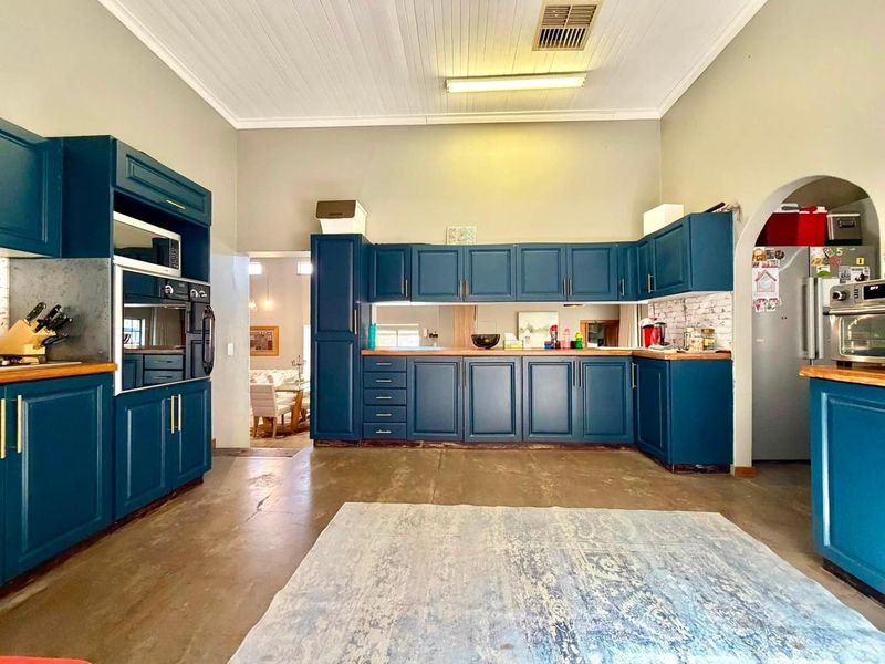 Spacious kitchen featuring deep blue cabinetry, timber countertops, a mirrored splashback, and high ceilings with exposed concrete flooring.