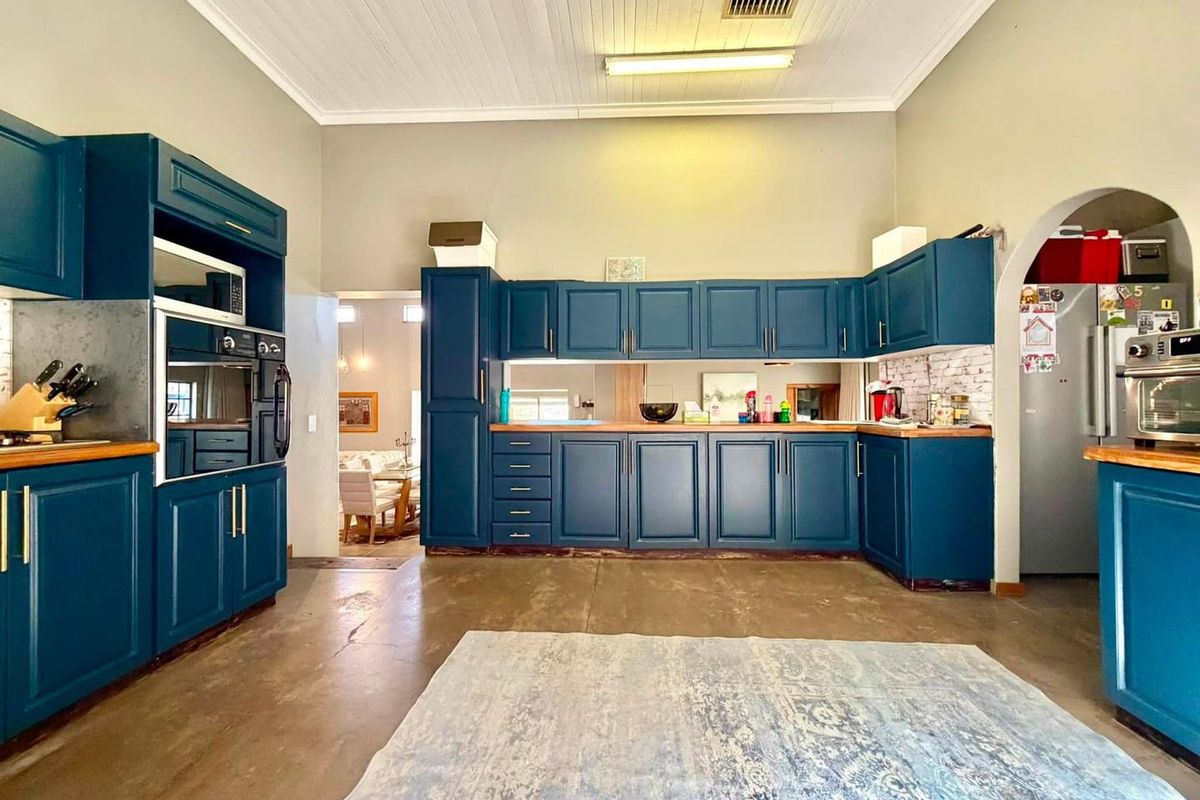 Spacious kitchen featuring deep blue cabinetry, timber countertops, a mirrored splashback, and high ceilings with exposed concrete flooring.