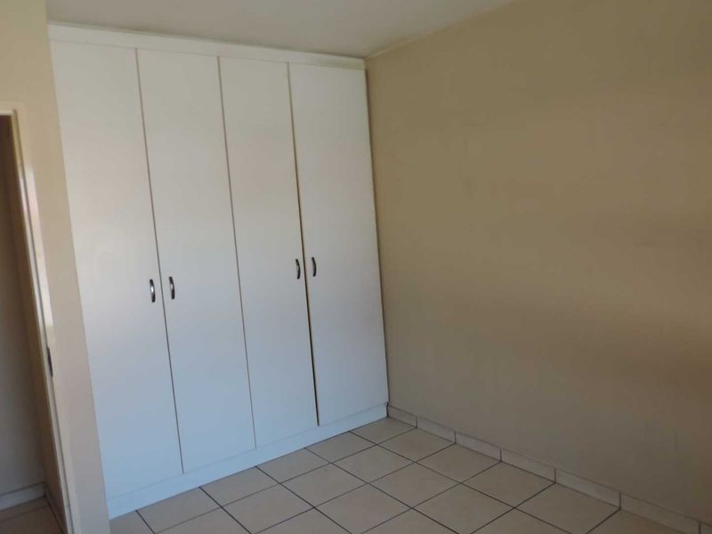A clean, empty bedroom featuring neutral wall paint, tiled flooring, and white built-in cupboards providing ample storage space.