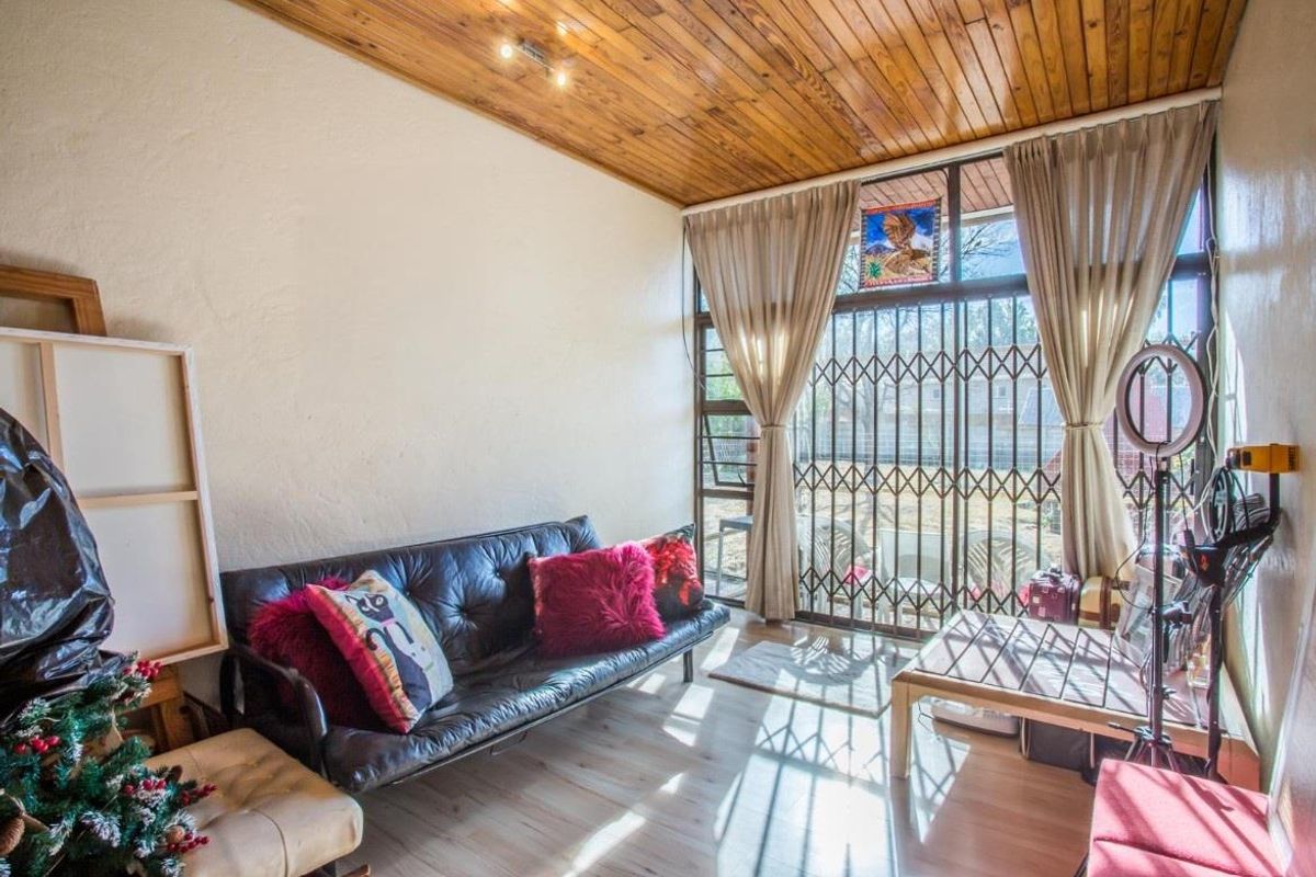 A living room featuring a timber-clad ceiling, large windows with security gates, and light-toned flooring, offering a bright and functional living space.