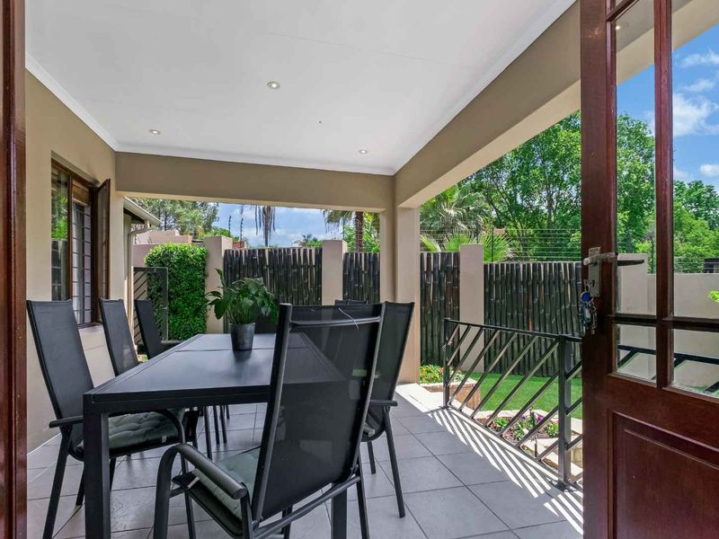 A covered outdoor patio featuring tiled flooring, recessed lighting, and a metal balustrade, providing a seamless transition to the garden area.