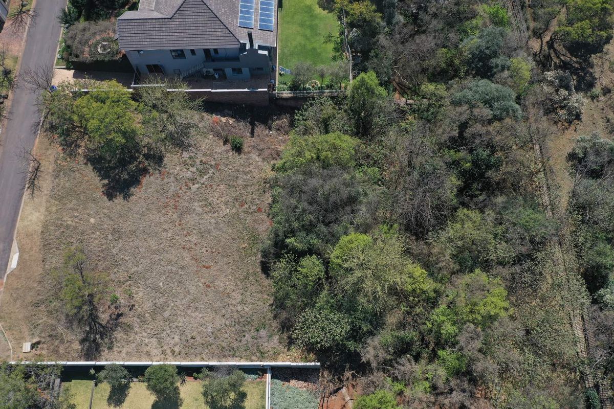 Aerial view of a vacant residential plot featuring established trees and direct street access, situated adjacent to existing residential properties.