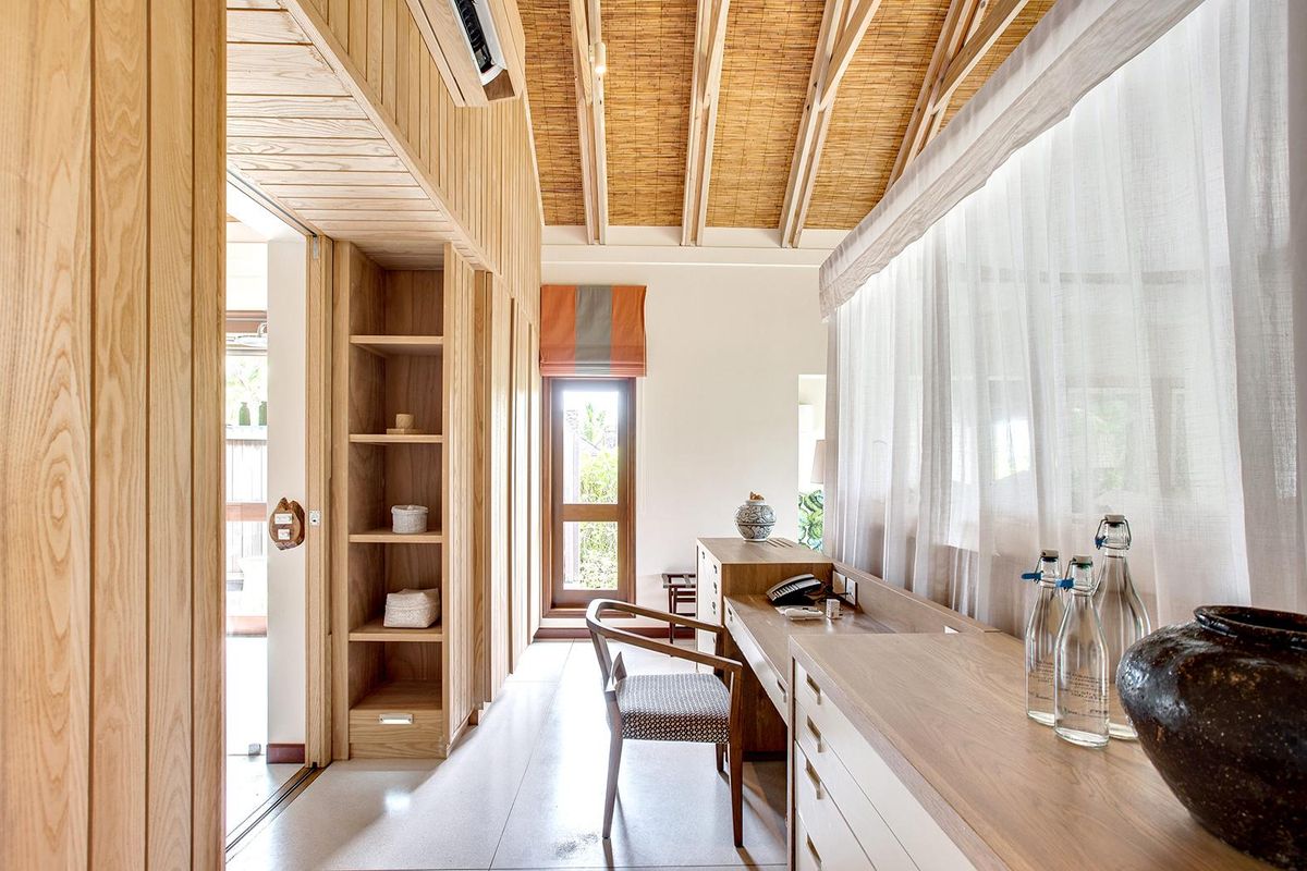 A well-appointed bedroom featuring custom timber cabinetry, a vaulted ceiling with natural textures, and integrated air conditioning in a modern villa setting.