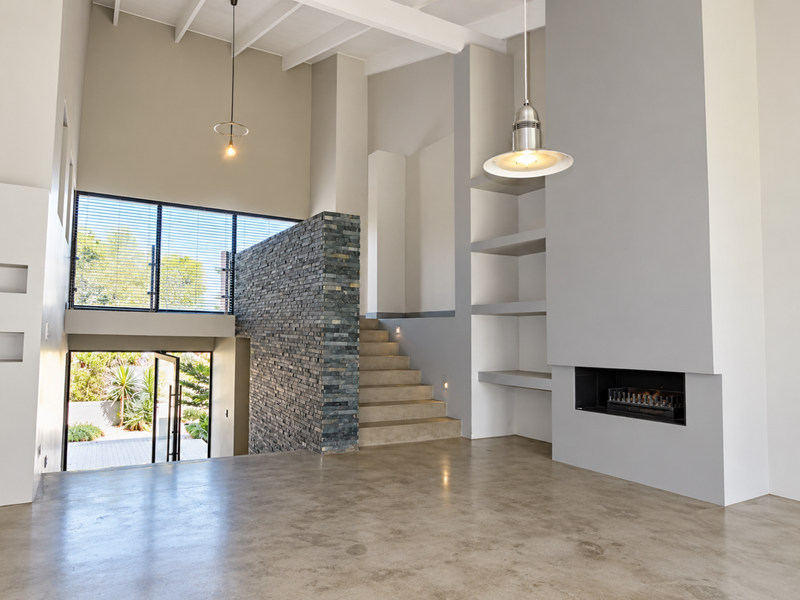 Spacious living area featuring high ceilings, a striking stone feature wall, built-in fireplace, polished concrete floors, and integrated shelving.