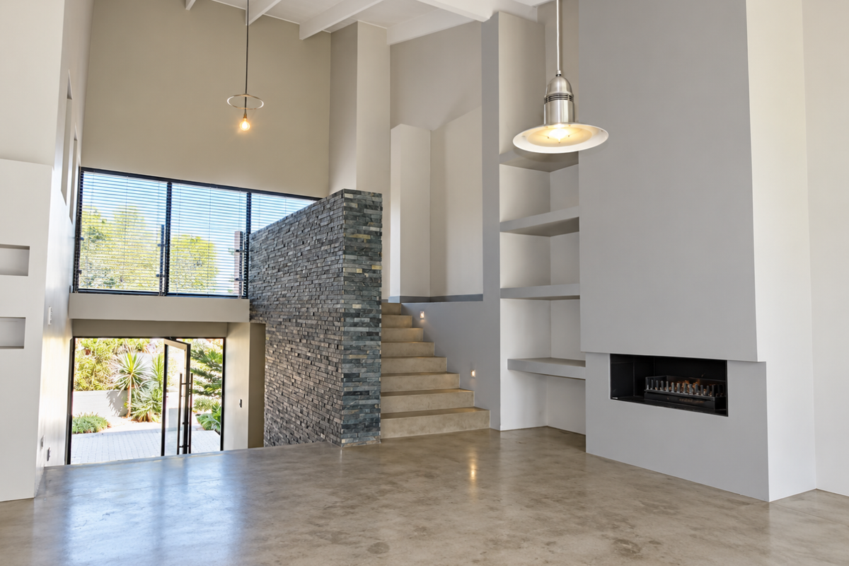 Spacious living area featuring high ceilings, a striking stone feature wall, built-in fireplace, polished concrete floors, and integrated shelving.