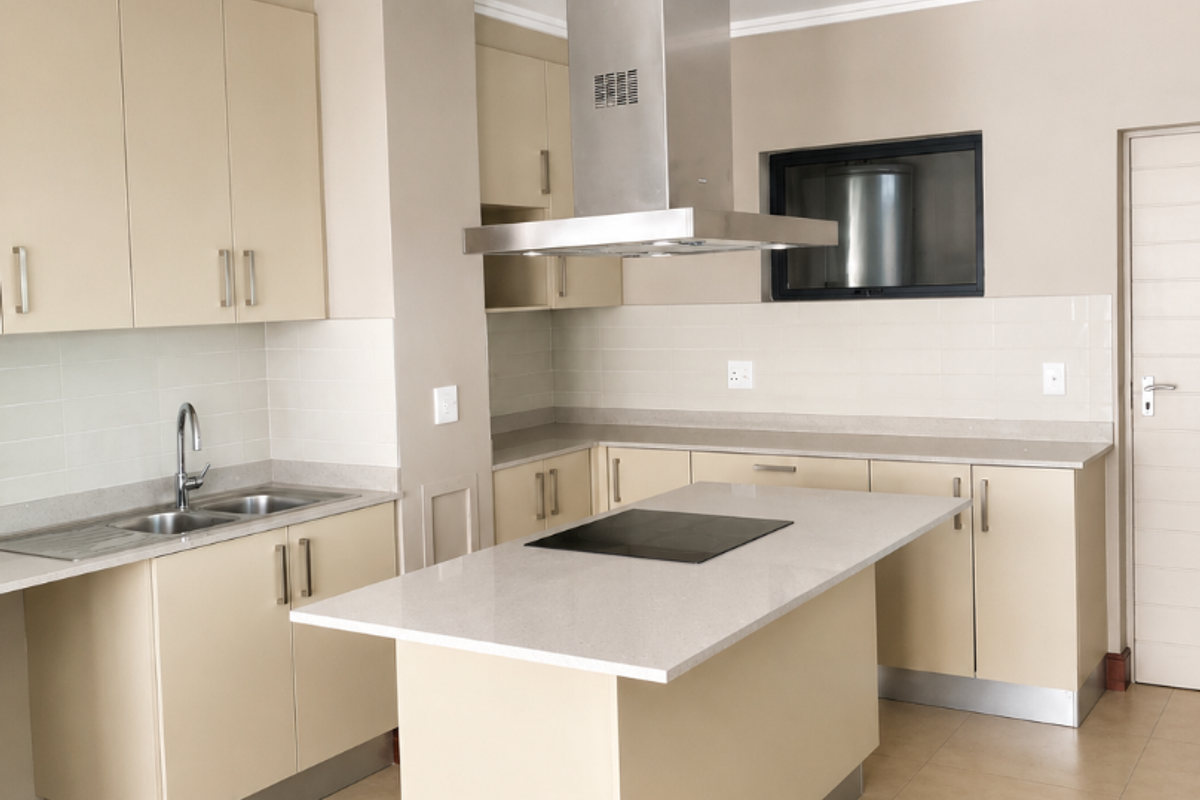 Modern kitchen featuring a central island with an integrated cooktop, stainless steel extractor fan, ample cabinetry, and neutral tiled flooring.