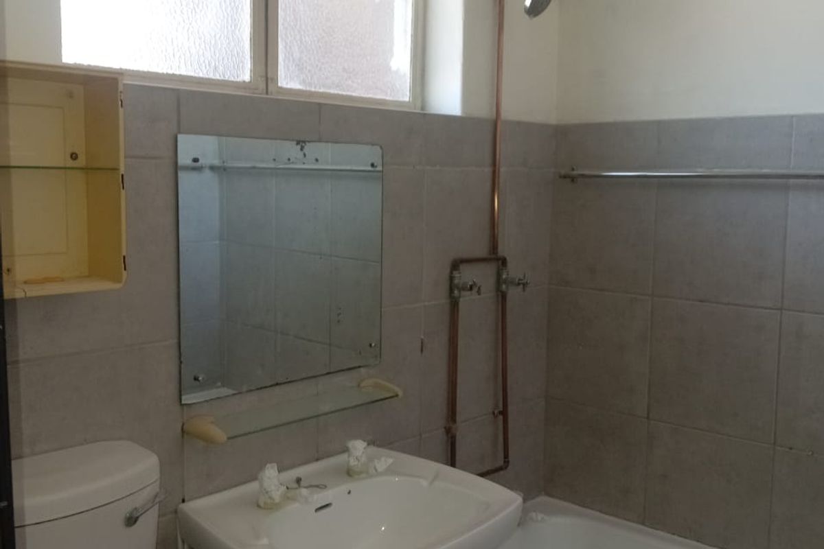 A dated bathroom featuring a pedestal basin, bathtub with exposed copper shower plumbing, and tiled walls, offering significant potential for modernization.