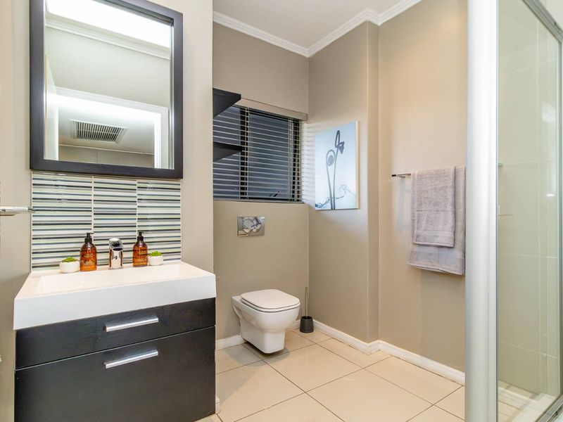 Modern bathroom featuring a sleek vanity with basin, wall-hung toilet with concealed cistern, and a glass-enclosed shower with neutral tiled finishes.