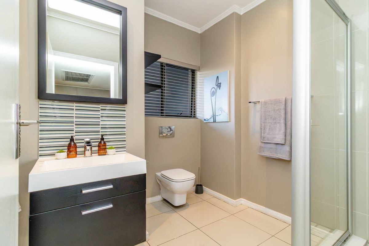 Modern bathroom featuring a sleek vanity with basin, wall-hung toilet with concealed cistern, and a glass-enclosed shower with neutral tiled finishes.