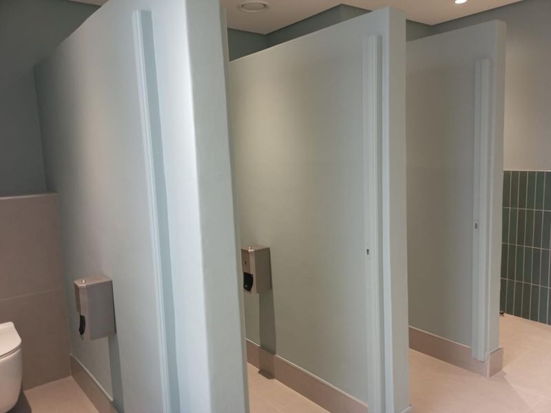 Modern commercial bathroom facility featuring multiple private toilet cubicles with clean finishes and wall-mounted dispensers.