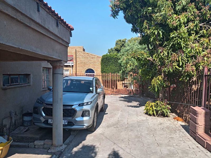 Front exterior view of the property featuring a paved driveway, covered patio area, and secure perimeter fencing.