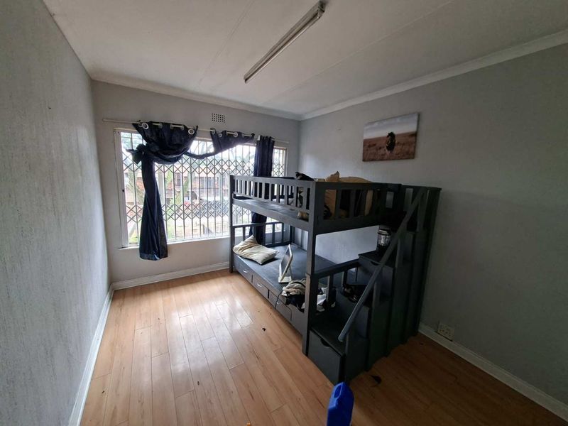 A bedroom featuring laminate flooring and security bars on the window, requiring minor cosmetic updates to improve its overall appeal.