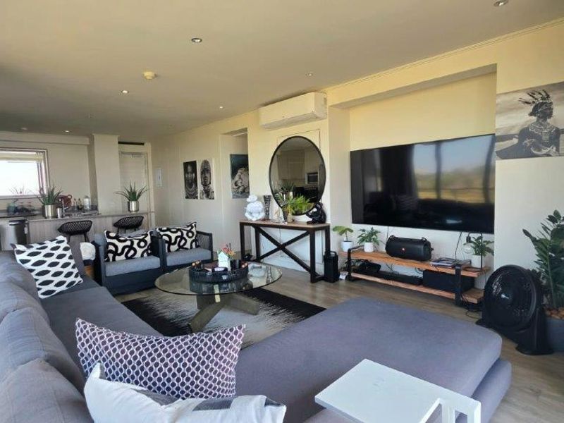 Spacious open-plan living area featuring laminate flooring, recessed lighting, a wall-mounted air conditioner, and an integrated kitchen space with modern cabinetry.