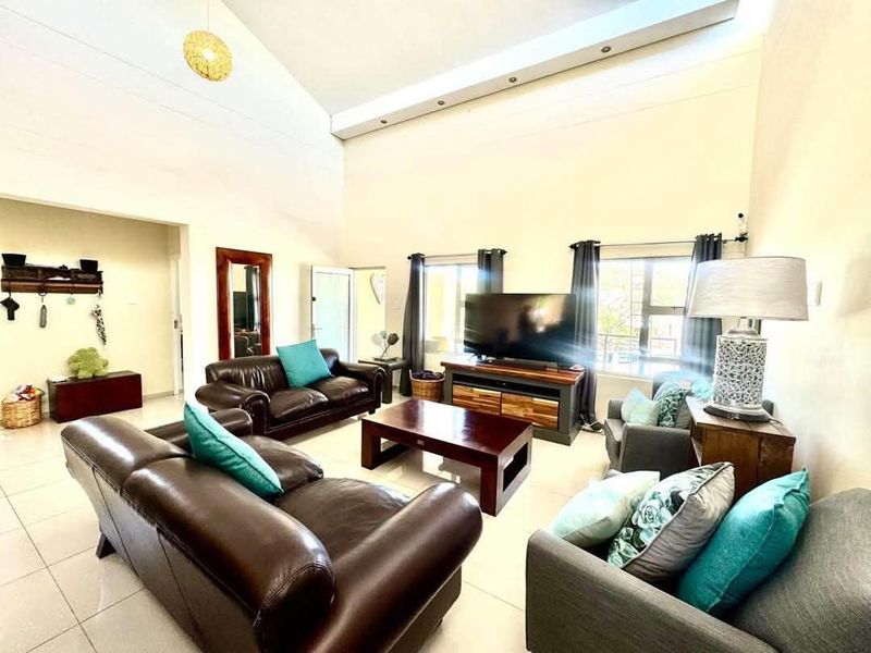 Spacious living room featuring high vaulted ceilings, tiled flooring, and abundant natural light from large windows, creating an open and airy atmosphere.
