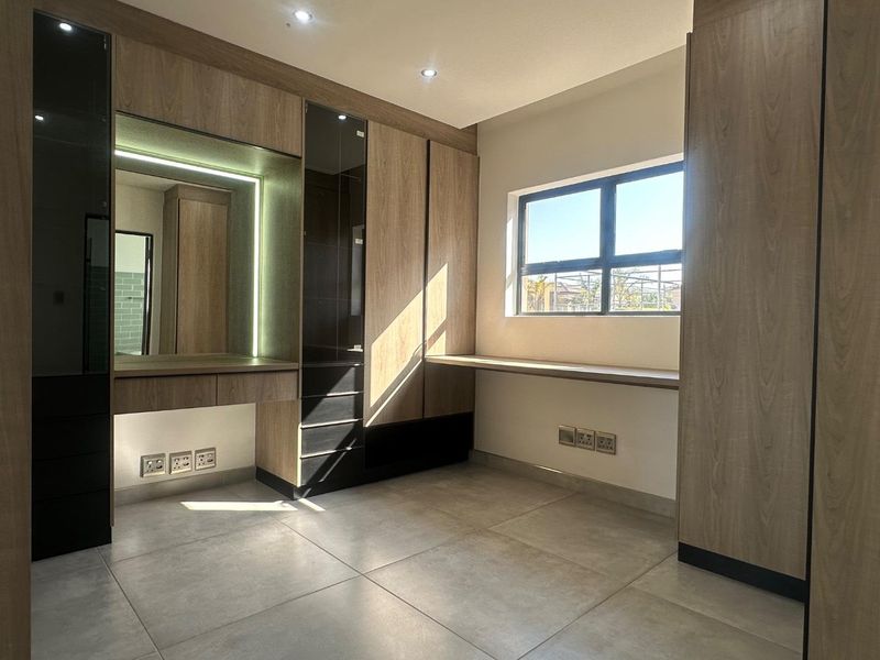 Modern bedroom featuring extensive built-in cabinetry, a dedicated vanity area with integrated lighting, a built-in desk, and large format floor tiles.