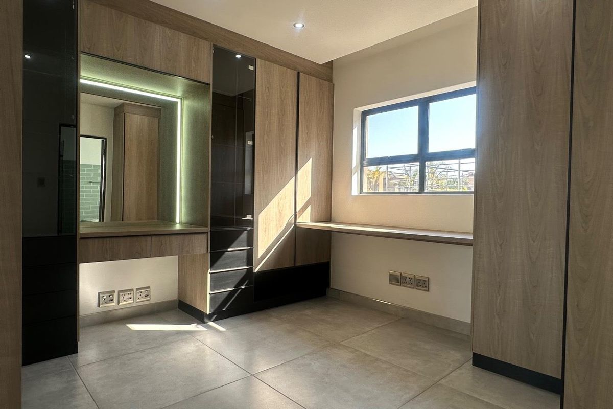 Modern bedroom featuring extensive built-in cabinetry, a dedicated vanity area with integrated lighting, a built-in desk, and large format floor tiles.
