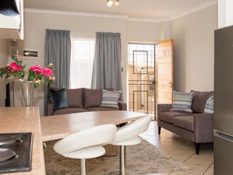 Open-plan living and kitchen area featuring tiled flooring, a breakfast counter with hob, and direct access to the exterior via a security gate.