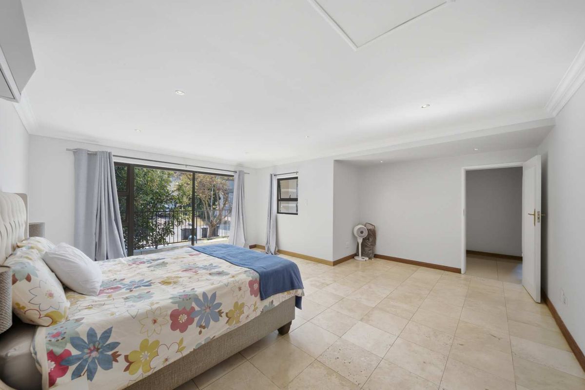 Spacious bedroom featuring neutral travertine tile flooring, recessed lighting, and large sliding glass doors providing access to a private balcony.