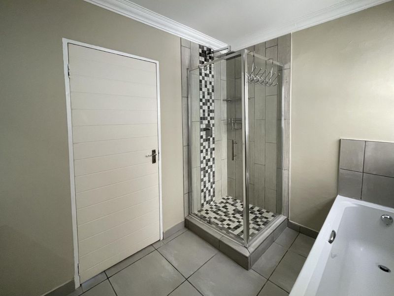 A clean bathroom featuring a glass shower enclosure with mosaic tile accents, a built-in bathtub, and neutral wall finishes.