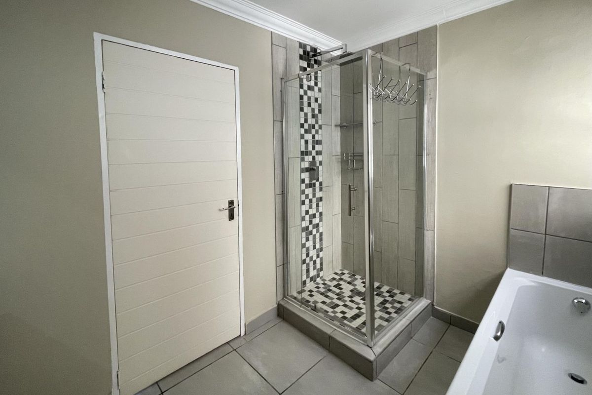 A clean bathroom featuring a glass shower enclosure with mosaic tile accents, a built-in bathtub, and neutral wall finishes.
