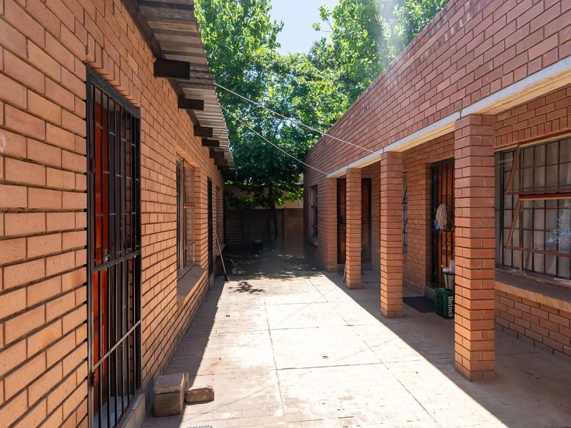 A covered outdoor walkway featuring exposed brick walls, brick pillars, and paved flooring, providing access between sections of the property.
